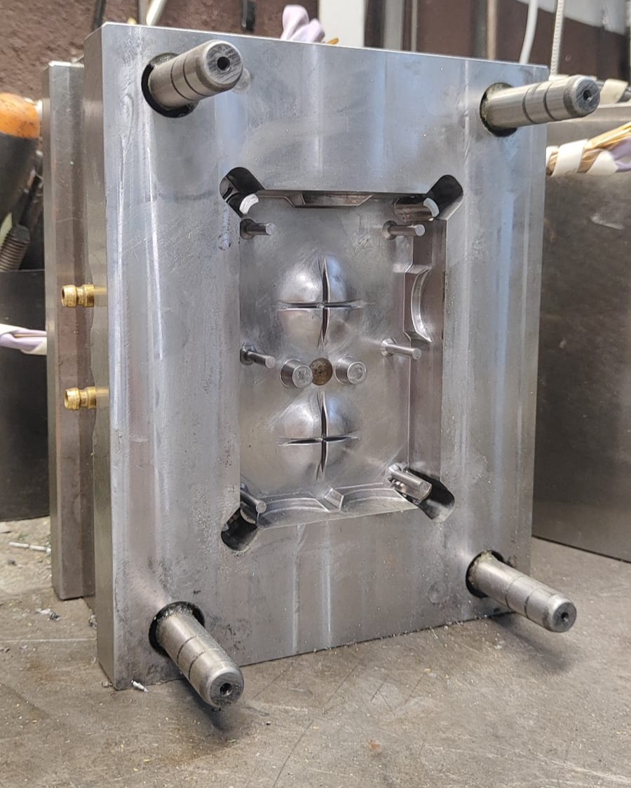 Metal injection-molding tool cavity with recessed impressions and locator pins on a workshop bench