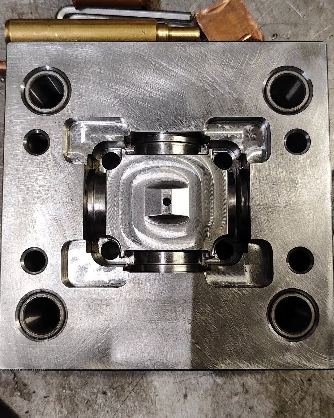 Square steel mold insert with central cavity and guide-pin holes, machined on a CNC mill, used in high-precision industrial applications