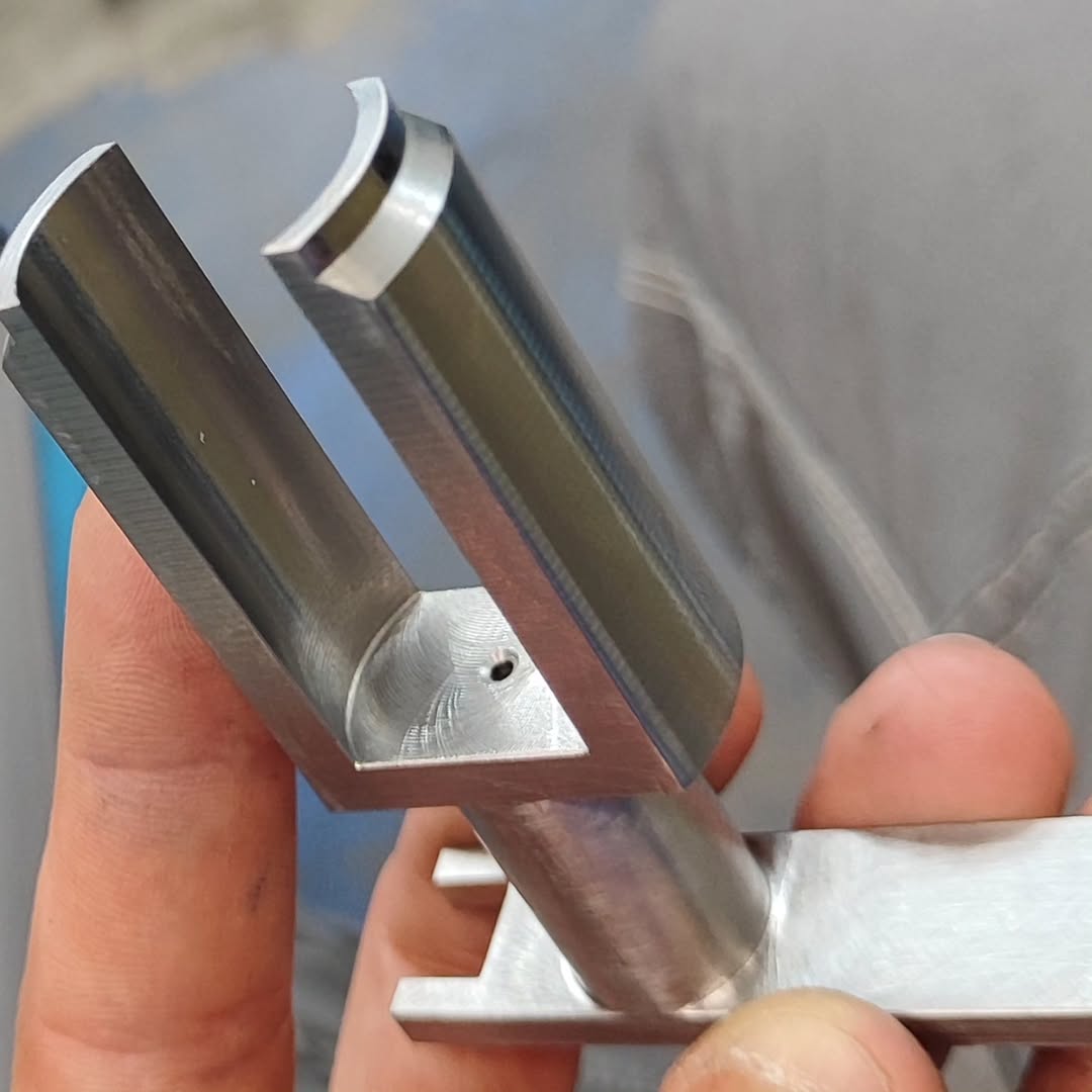 Close-up of a freshly milled aluminum bracket with a U-shaped pocket and cylindrical boss, held by a person's hand