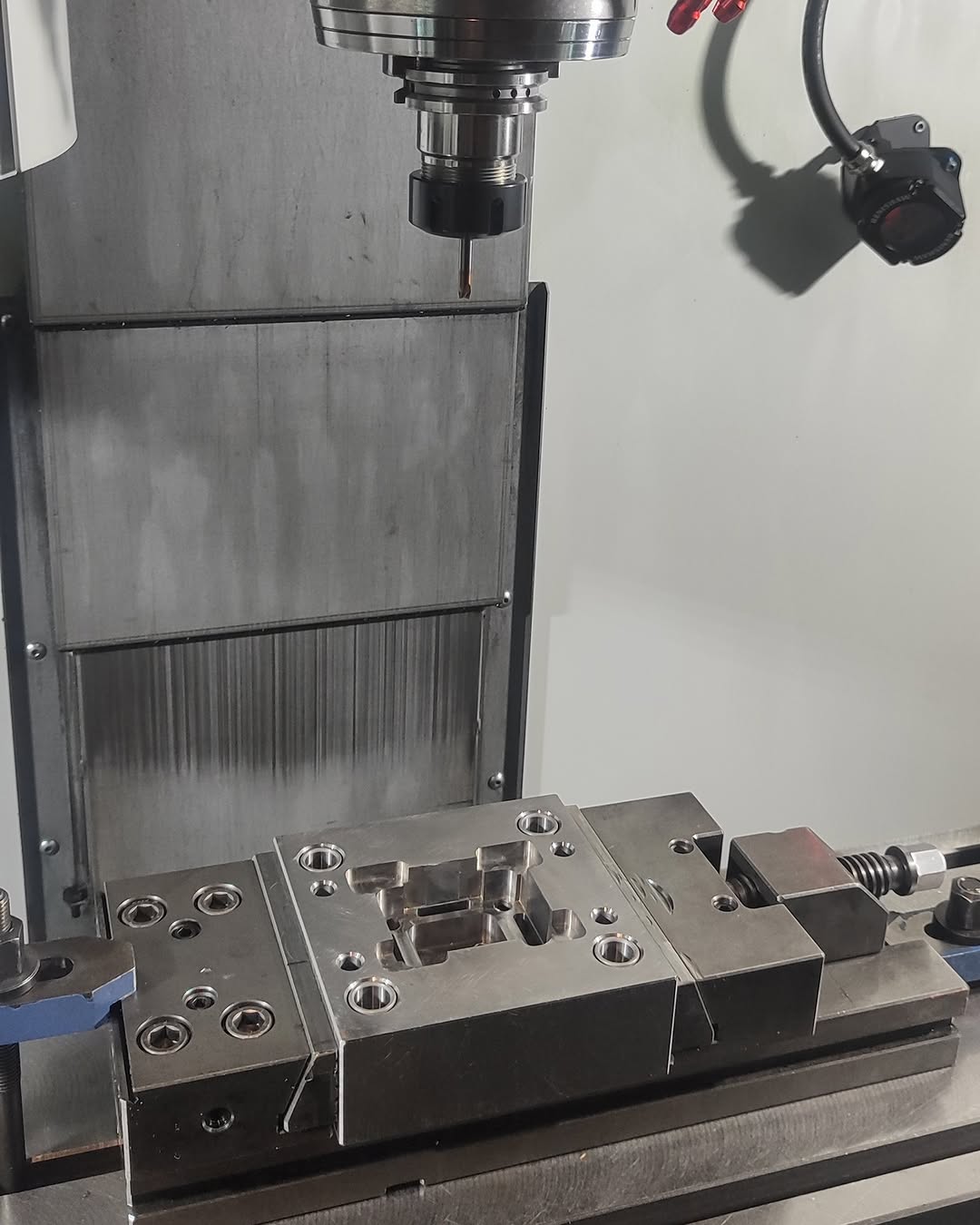 Metal block secured in CNC milling machine with endmill tool overhead