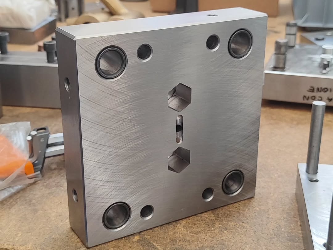Square steel tool block with bearing bushings and hexagonal cutouts on a workbench