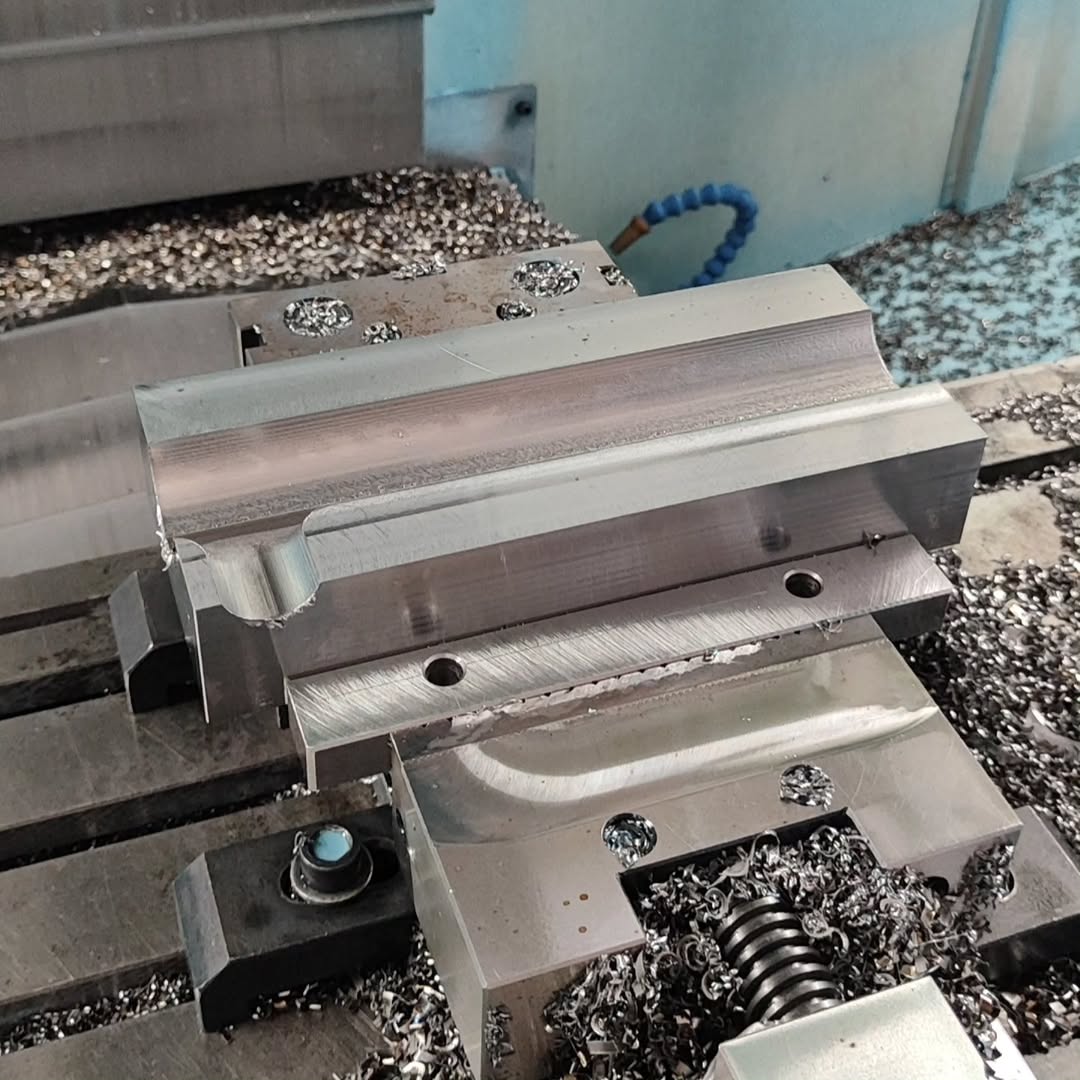 Metal workpiece clamped in a vise on a CNC milling machine bed with scattered swarf and chips