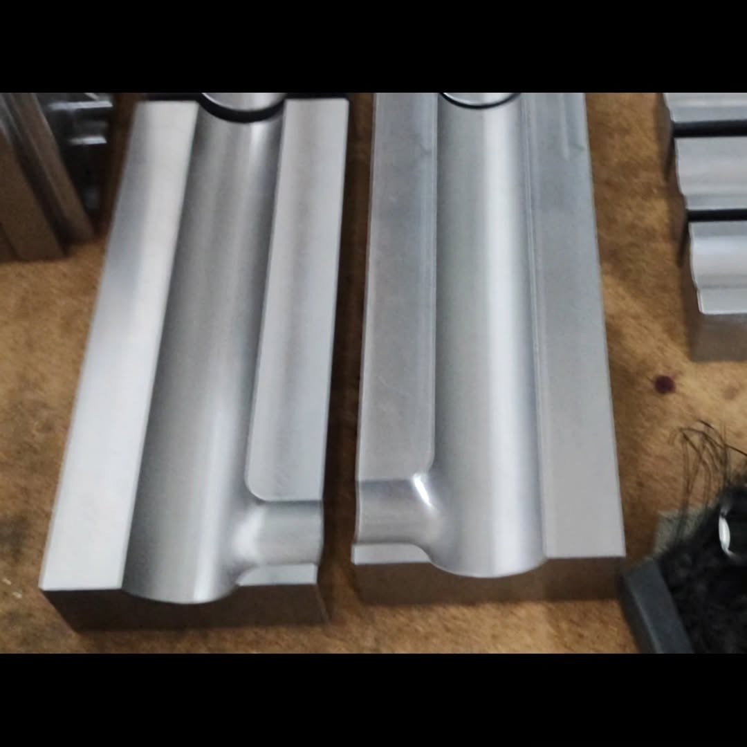 Two polished metal mold halves with precisely milled cavities on a workshop bench