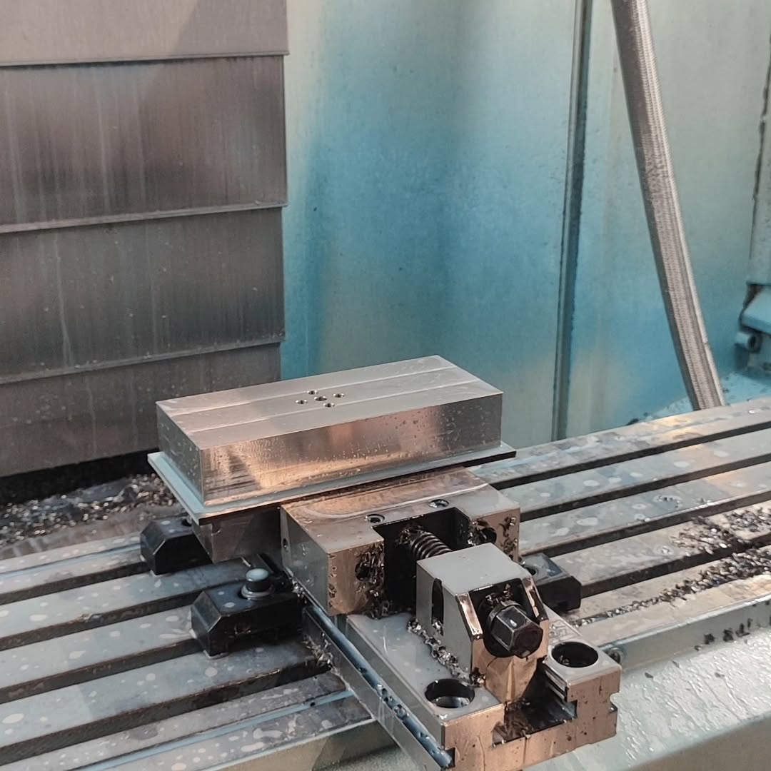Metal billet clamped in CNC milling machine with drilled holes and milled faces