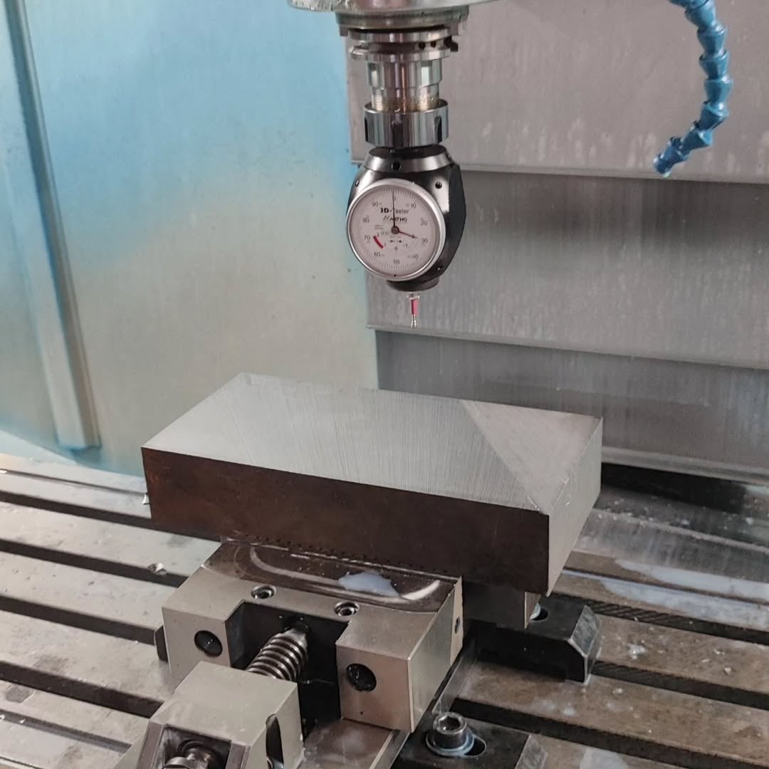 Metal block clamped in CNC milling machine with dial indicator for setup and alignment