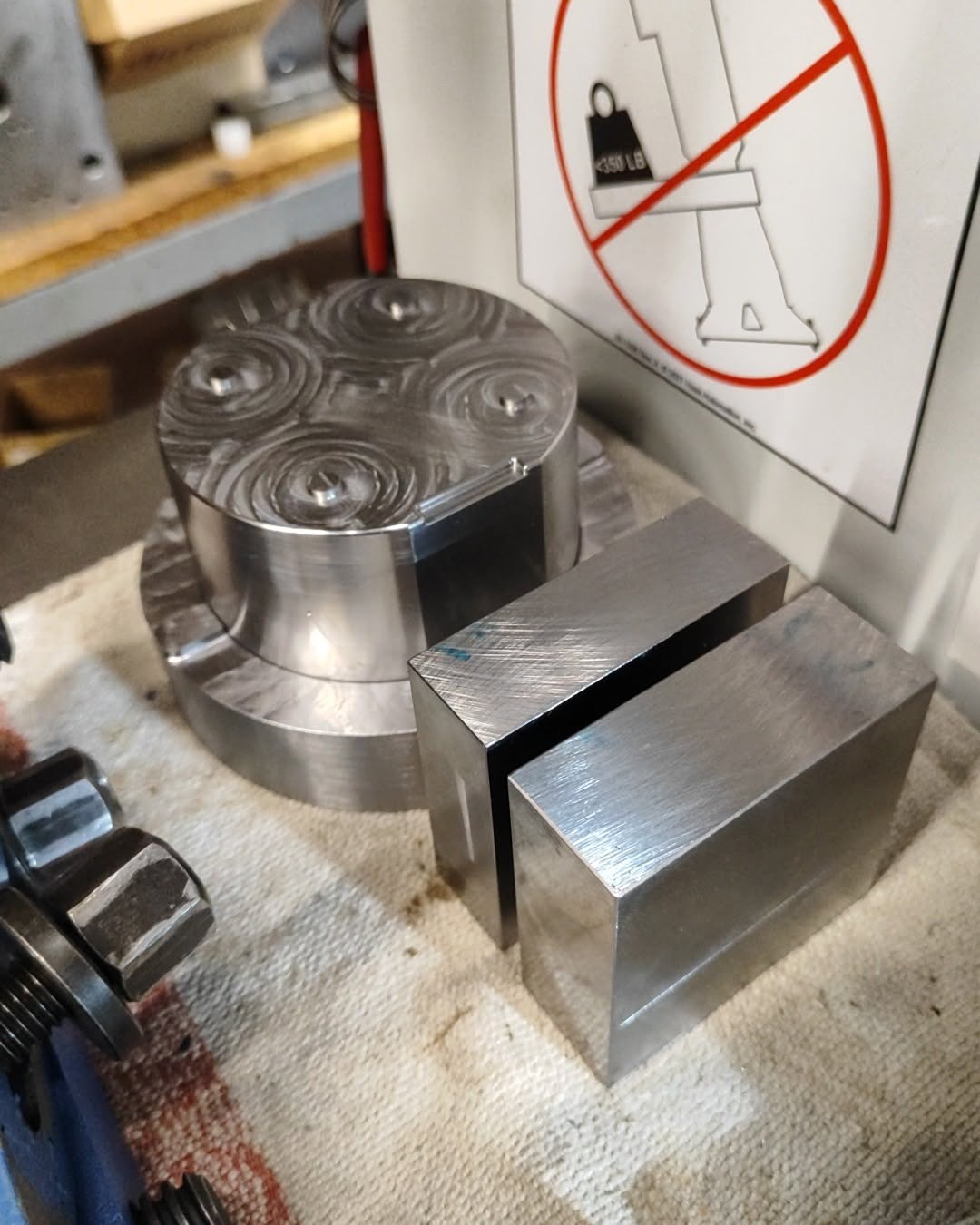 Circular metal blank with concentric tool-path marks and rectangular blocks on CNC milling machine table