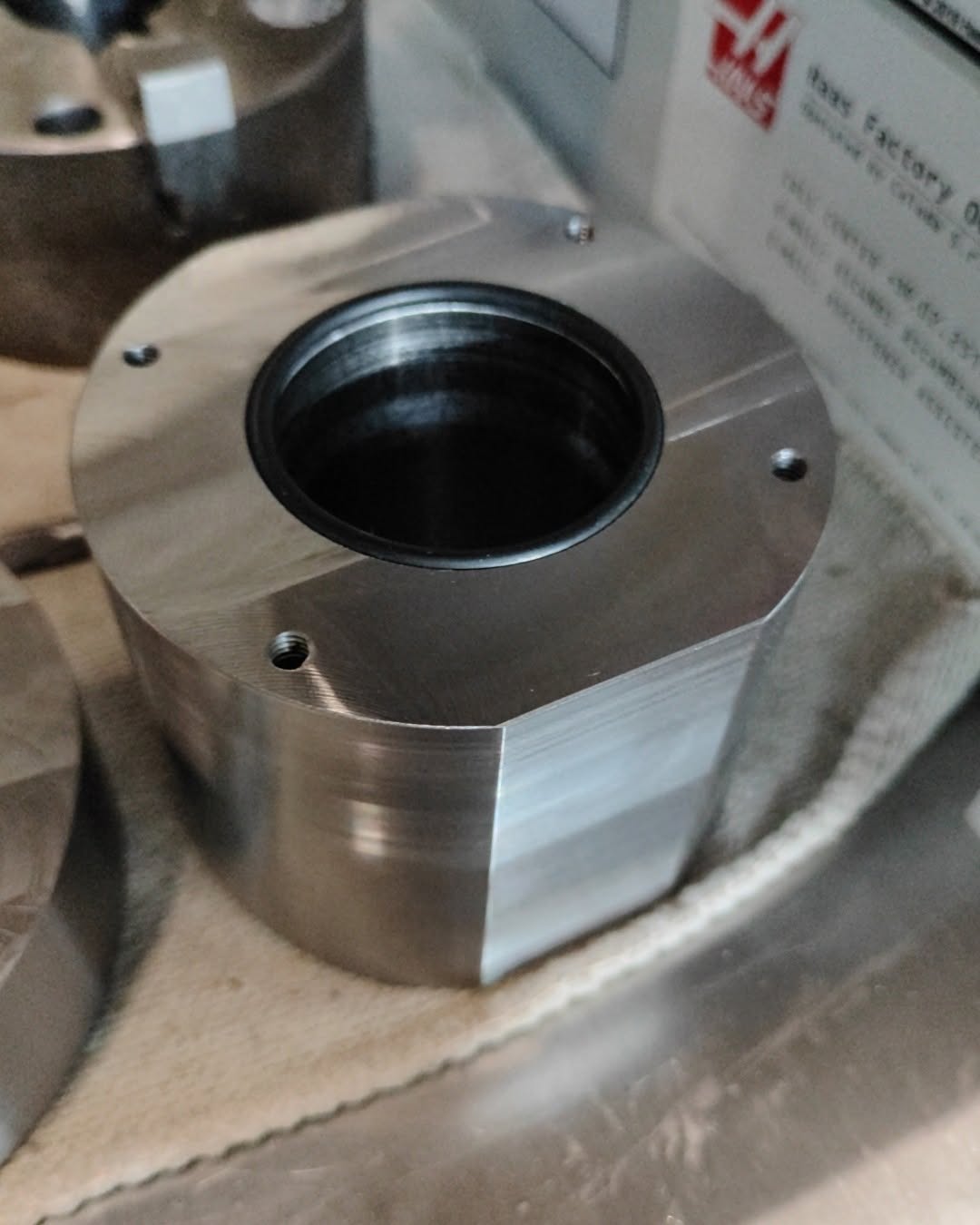 Metal housing with cylindrical bore and bolt holes on shop cloth inside a Haas CNC mill enclosure