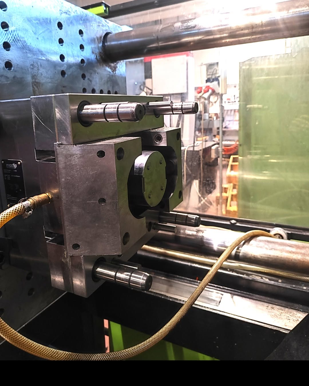 Close-up of a steel mold half seated in a horizontal injection-molding machine's clamping unit, with guide pillars and a circular cavity for plastic parts