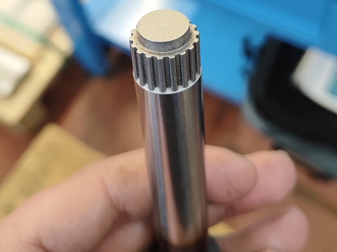 Hand holding a machined metal spline shaft with external teeth and smooth cylindrical body