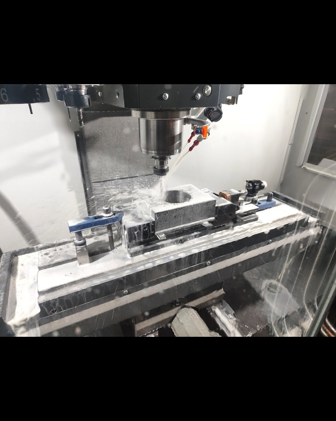 Vertical CNC milling machine cutting a circular pocket in a metal block with coolant spray