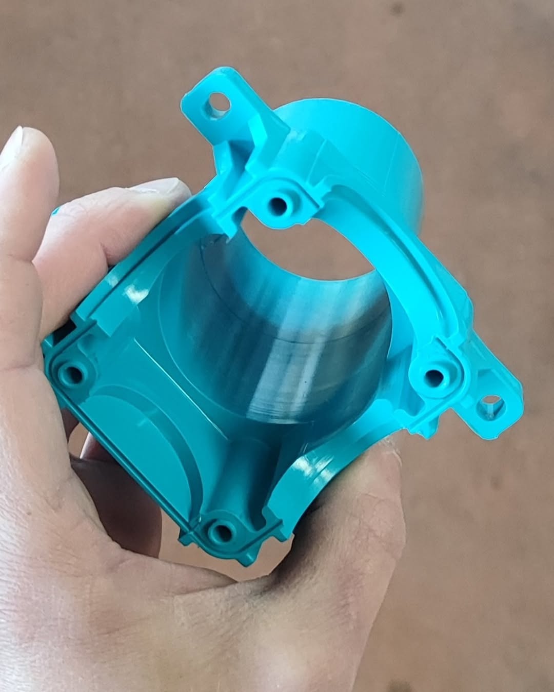 Bright cyan cylindrical housing with mounting lugs and precision-machined bores, produced via CNC milling