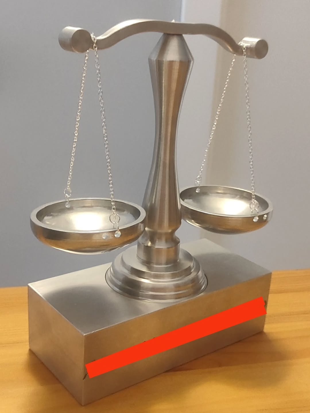 Polished metal double-pan balance scale mounted on a rectangular base