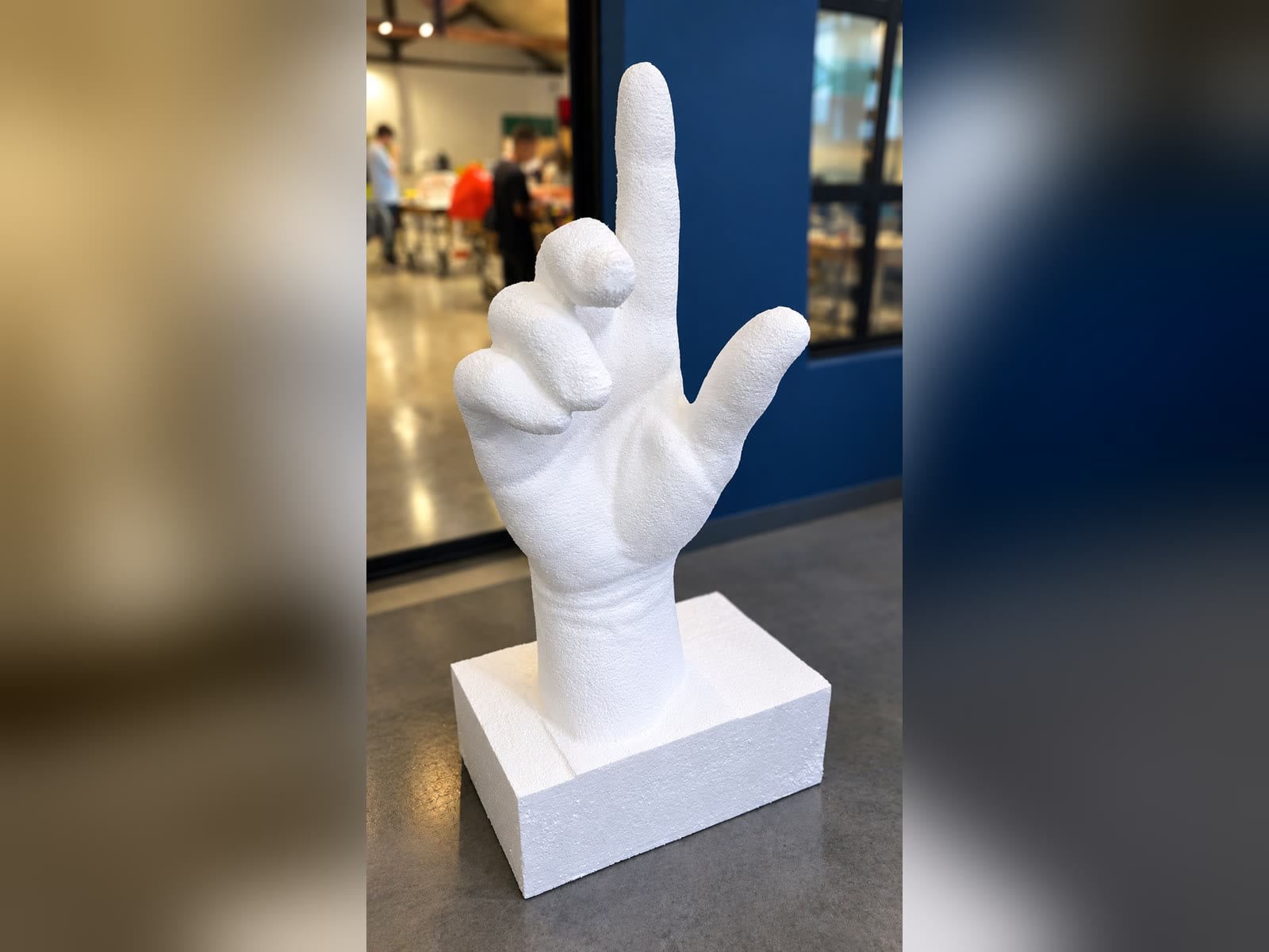 Finished white foam hand sculpture with raised index finger on a base