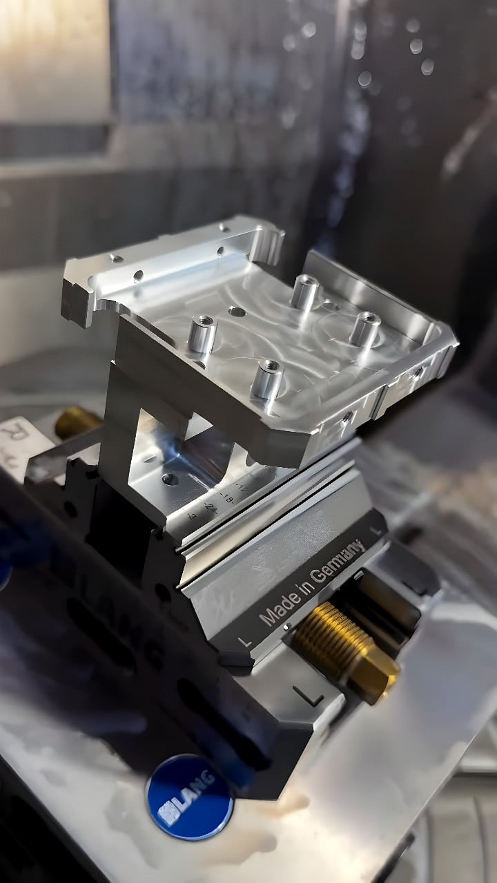 LANG 'Made in Germany' CNC vise holding an aluminum workpiece with raised cylindrical bosses and scalloped toolpath marks inside a milling center