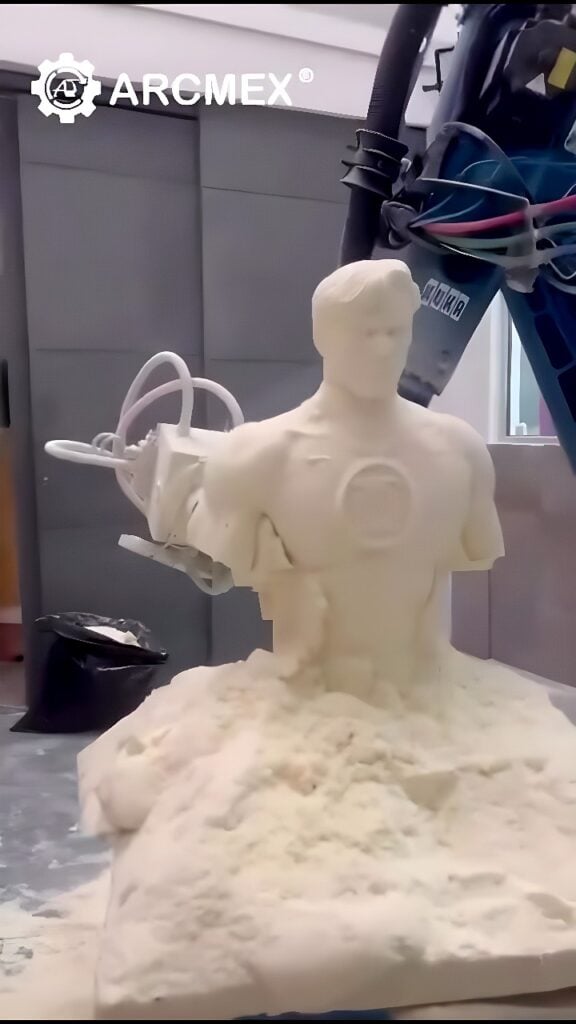 Six‑axis industrial robot CNC‑milling a white foam Iron Man torso bust with a rotating end‑mill and foam chips at the base