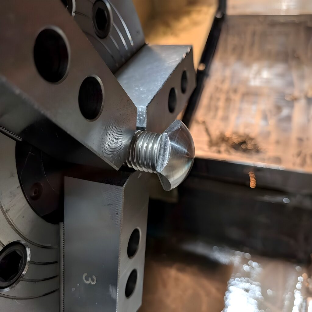 A four-jaw CNC lathe chuck holding a cylindrical metal blank during external threading, with metal swarf and coolant visible.