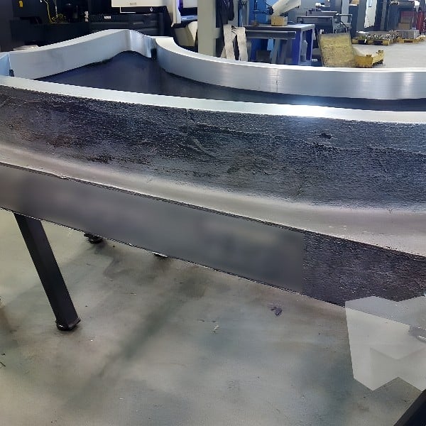 Large curved aluminum casting being machined on a CNC milling center with industrial robot in background