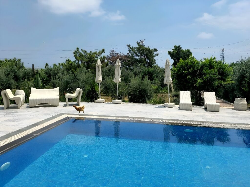 Set of four white, sinuous-layered outdoor furniture pieces including armchairs, sofa, low table, and planter, arranged on concrete slab