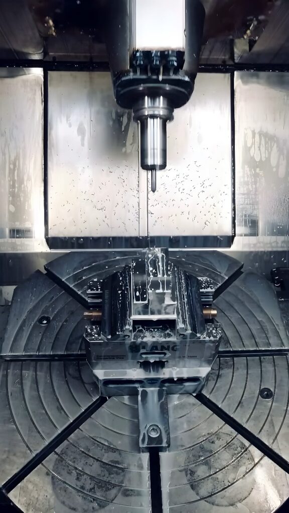 Vertical CNC machining center milling a metal workpiece with coolant and rotary table