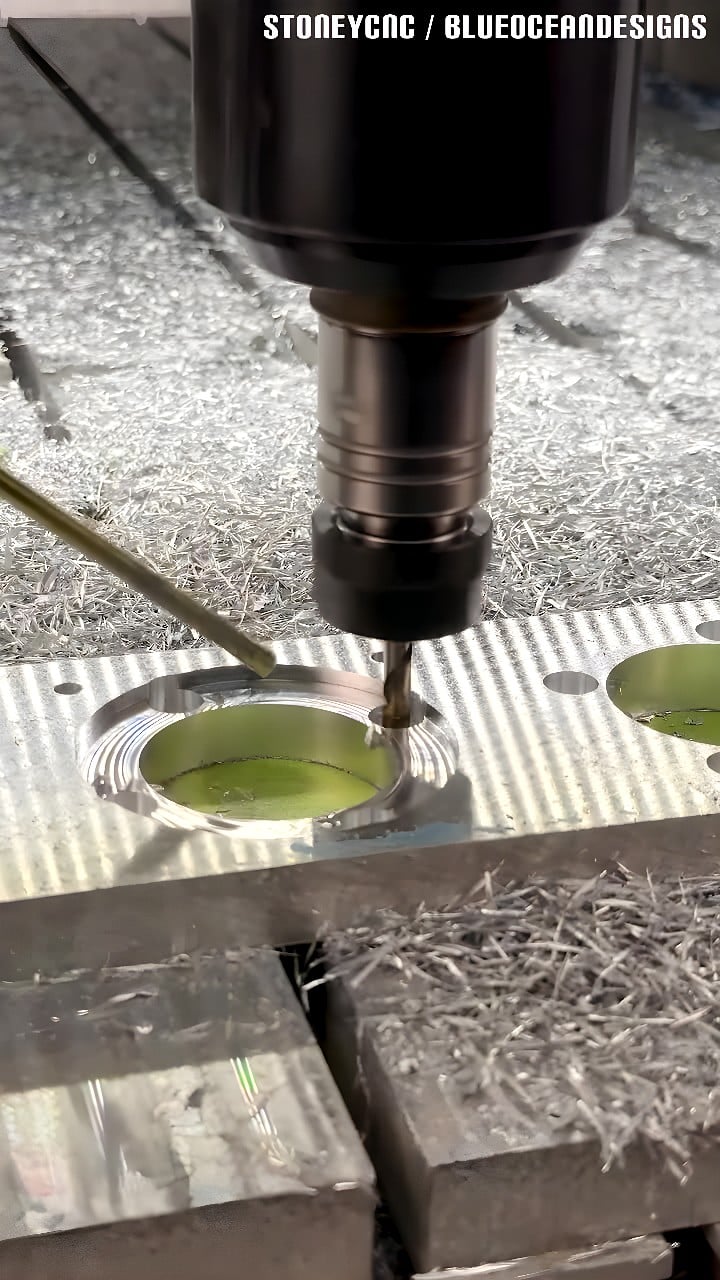 Vertical CNC milling spindle pocket-milling circular cavities into an aluminum plate, coolant applied and aluminum chips around the recesses