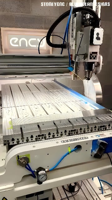 Gantry-style CNC milling machine face-milling parallel T-slot grooves in an aluminum plate secured on a vacuum table