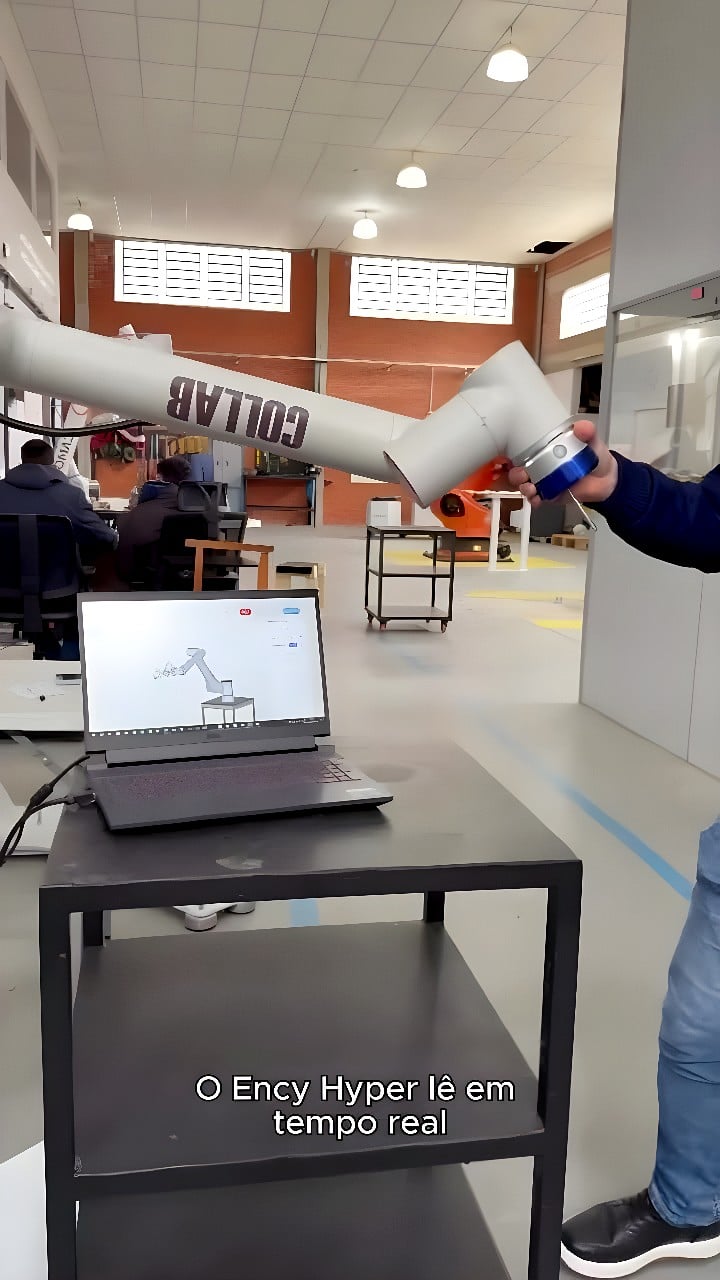 White collaborative 6-axis robot arm fitted with a blue force-torque sensor at its wrist, performing real-time force measurement with live data visible on a laptop screen.