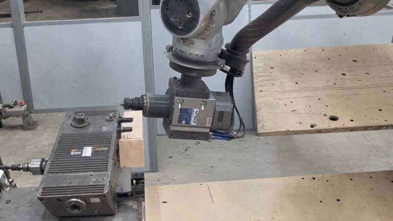 Six-axis industrial robot arm milling a wooden workpiece with CNC spindle, producing wood chips and sawdust