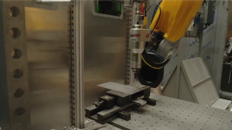 A six-axis industrial robot performing fiber-laser cutting on a metal plate inside a machining cell