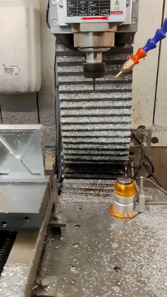 CNC milling machine machining a small cylindrical aluminum part with coolant and chips visible