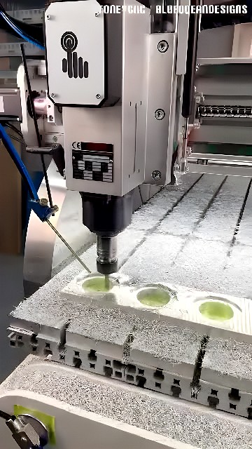 Vertical CNC milling head cutting circular pockets into an aluminum plate with metal chips around the work area