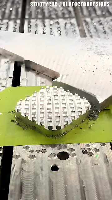 CNC milling end mill cutting a waffle-style grid pocket into an aluminum plate with green sacrificial backing and metal chips around the work area