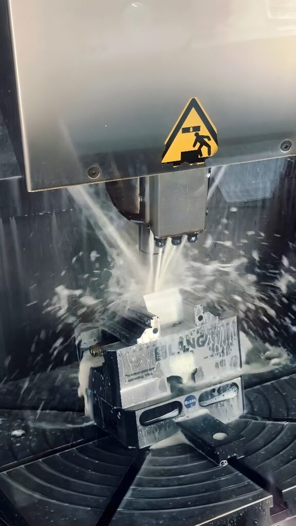 CNC vertical machining center cutting a white block with end mill and flood coolant