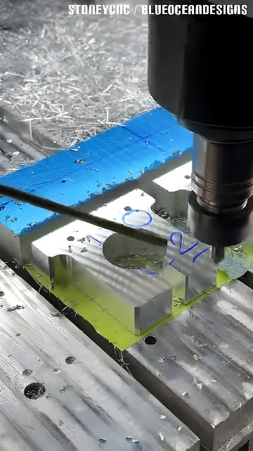 Vertical CNC milling center machining pockets and holes into an aluminum workpiece with metal chips and coolant visible