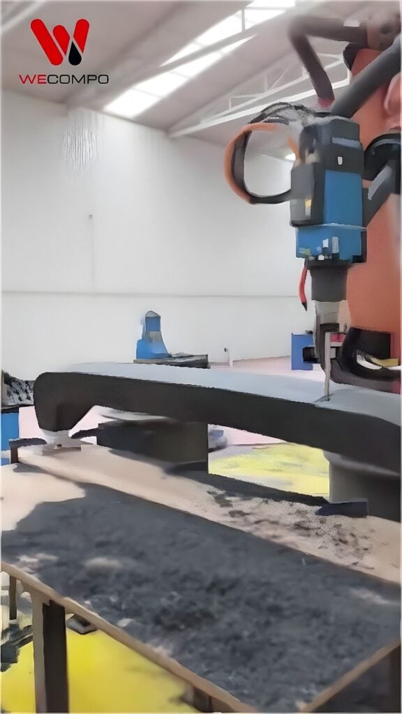 Six-axis industrial robot extruding black composite pellets onto a curved mold for pellet-based additive manufacturing
