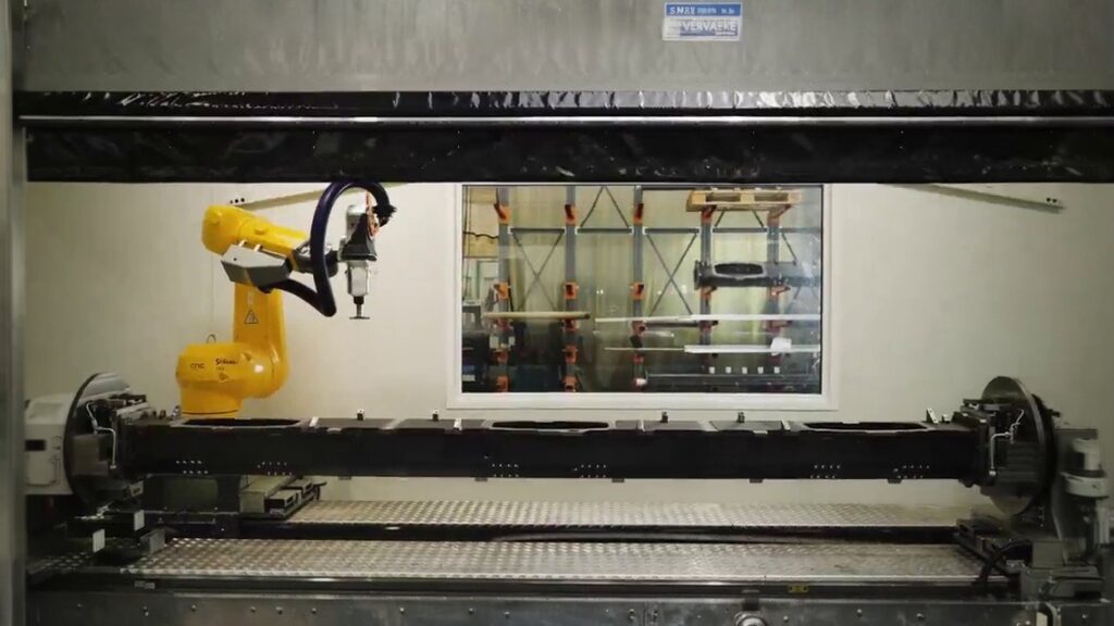 Yellow industrial robot machining a tubular metal workpiece inside an enclosed machining cell
