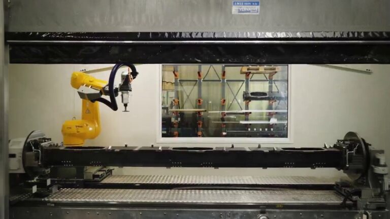 Yellow industrial robot machining a tubular metal workpiece inside an enclosed machining cell