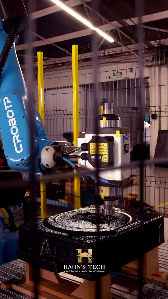Blue CROBOT robotic arm with milling spindle cutting a circular pocket into a black cast-metal workpiece inside a safety-fenced cell.