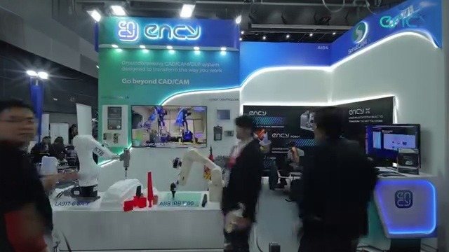 Two ABB IRB 1200 industrial robots mounted on a demo table, equipped with end-effectors, machining red plastic prototype parts in a trade-show setup.
