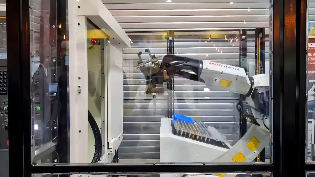 Six-axis industrial robot arm loading metal blanks into a CNC machining center in an automated manufacturing cell