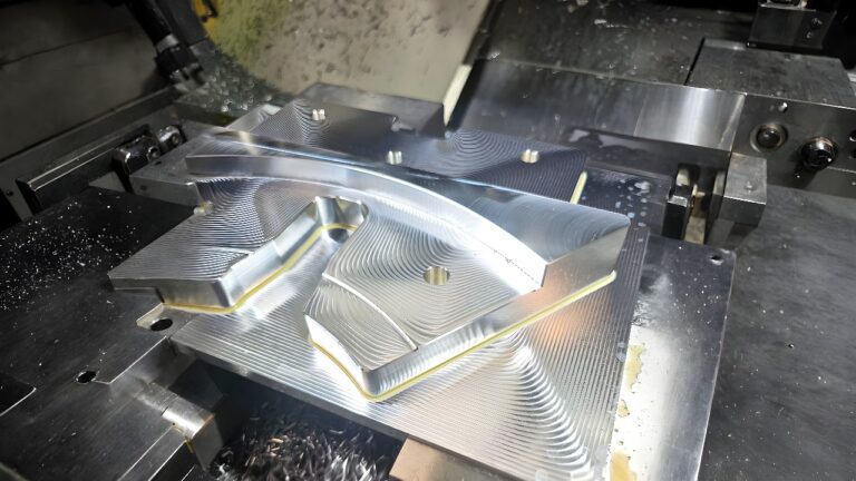 Aluminum blank clamped in a CNC milling machine vise with visible tool marks and metal chips