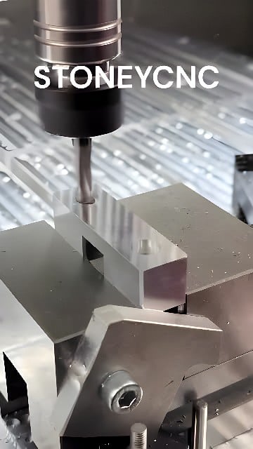 Vertical CNC milling machine cutting a rectangular aluminum block held in a precision vise with metal chips on the machine bed