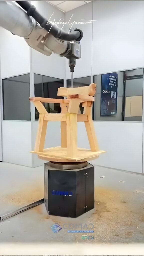 Six-axis industrial robot with a vertical milling spindle machining a solid wood chair blank on a powered rotary base