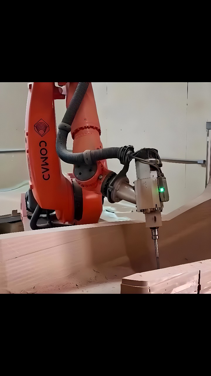 COMAU six‑axis industrial robot with a high‑speed milling spindle machining a solid wood block in a workshop
