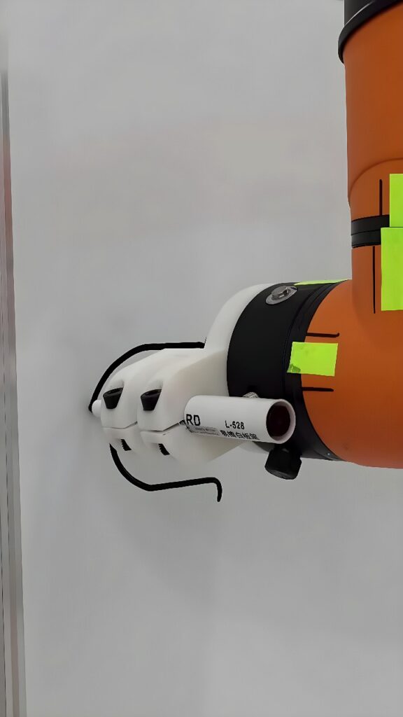 Orange collaborative robotic arm with a white three-fingered gripper holding a labeled PVC tube (RD L-528) aligned to a flat panel during an automated assembly operation.