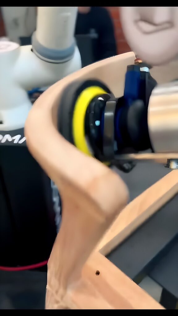 Collaborative robot arm sanding the curved edge of a wooden furniture frame