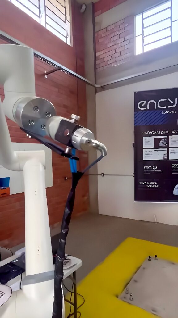 A six-axis collaborative robot arm with a MIG welding torch welding a steel plate on a yellow work surface