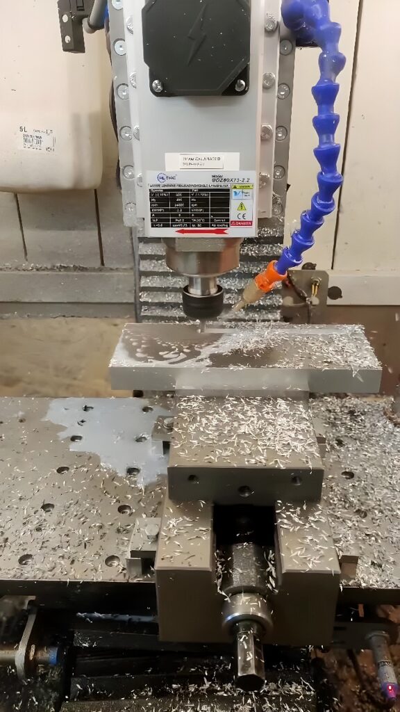 Vertical CNC milling machine face-milling an aluminum block with coolant applied