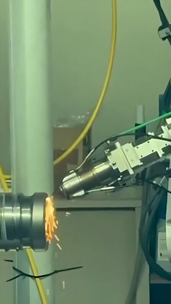 A multi-axis robotic arm with an abrasive spindle grinds the surface of a rotating steel cylinder, producing sparks in an automated industrial cell.
