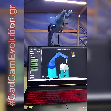 Six-axis industrial robot arm in a curtained workspace with a laptop displaying CAD/CAM software and toolpaths