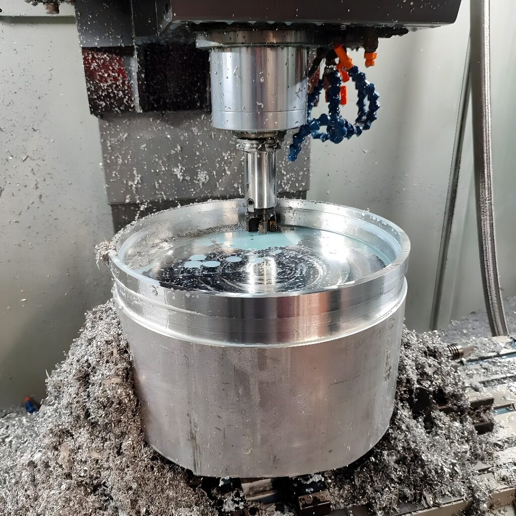 Vertical CNC milling machine actively machining a large cylindrical aluminum workpiece with metal chips and coolant visible